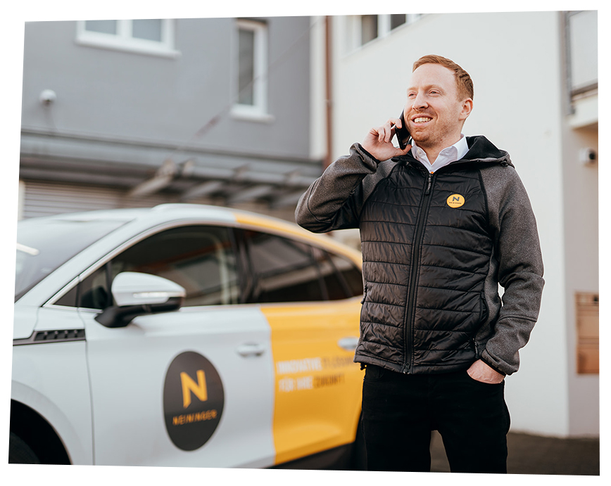Foto von Daniel der vor der Firma neben seinem folierten Auto ein Telefonat führt.