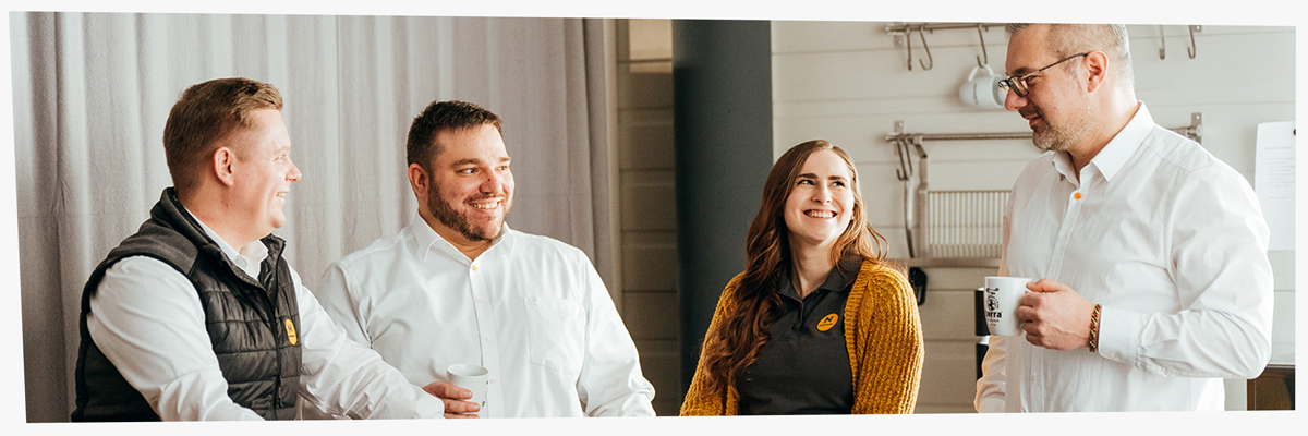 Breites Foto von 4 Personen die sich in der Kaffeepause unterhalten und gemeinsam lachen.